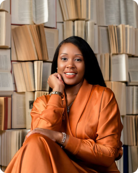 Headshot of Tatiana S. Richardson, LMSW. Smiling while sitting in front of a stack of books while wearing a burnt orange outfit.